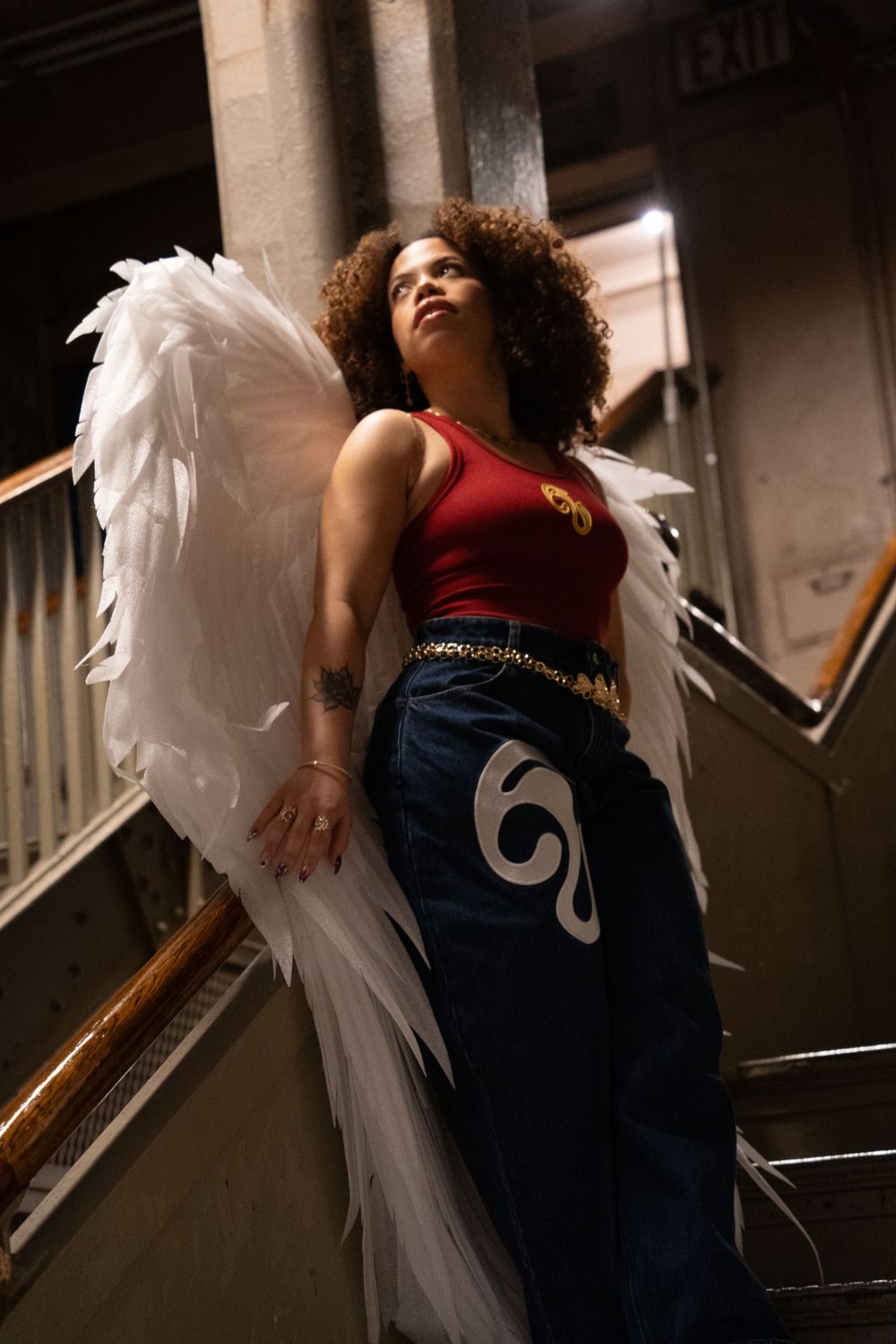Person with angel wings posing dramatically on stairs in casual attire.