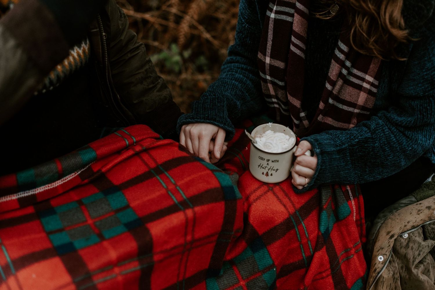 A close up of a couple holding hands. In their other hand they are holding mugs of hot chocolate.