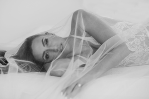 A soft black and white portrait of someone lying down in lace and tulle fabric with ethereal lighting.