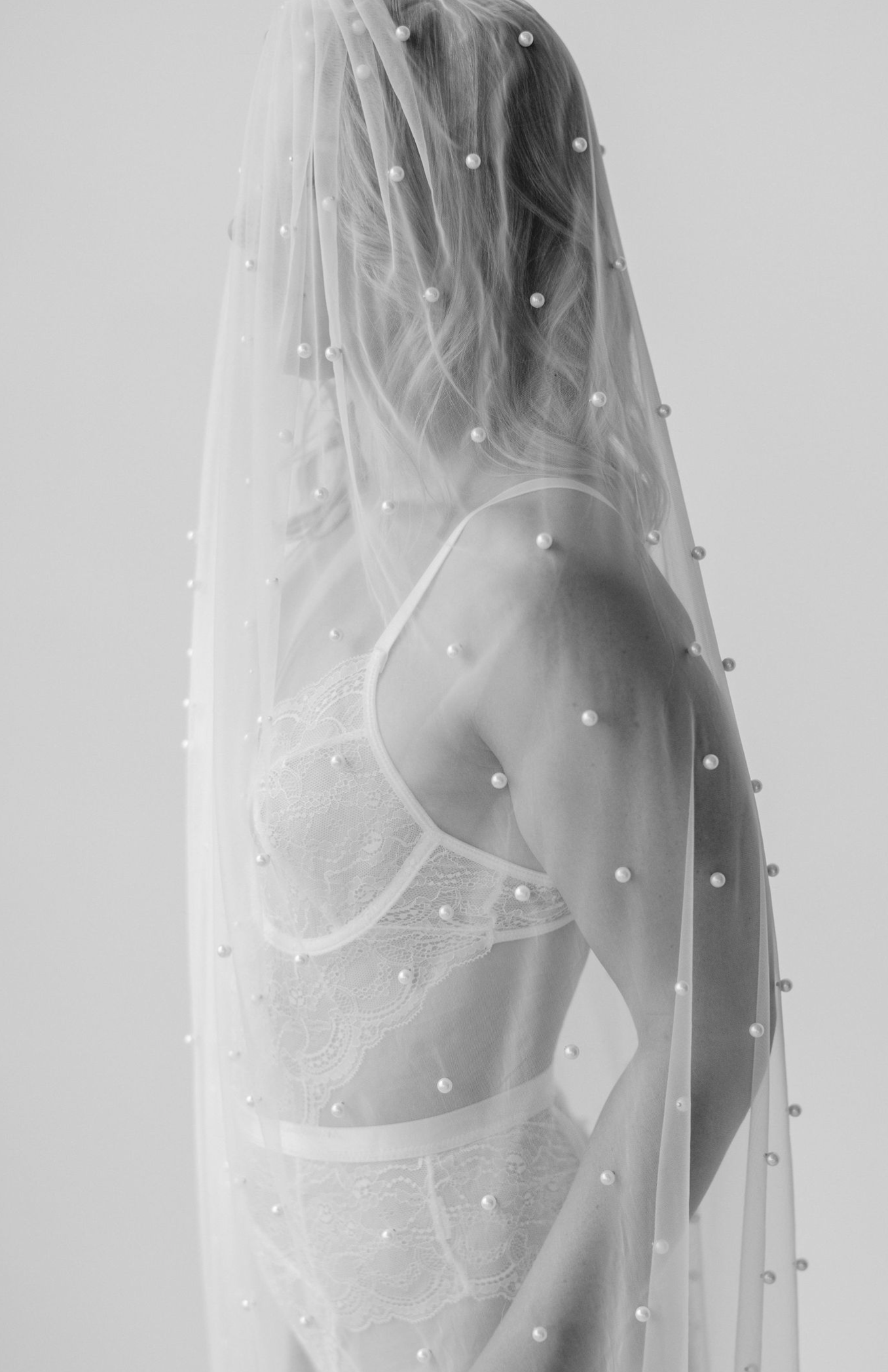 Black and white photo showing a silhouette through a sheer veil adorned with small pearl-like beads.
