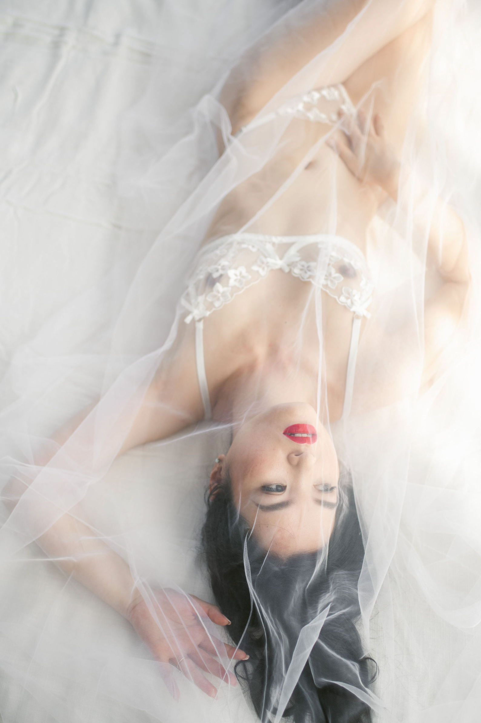 Dreamy boudoir photo with white tulle veil and delicate lace lingerie creating an ethereal romantic mood.