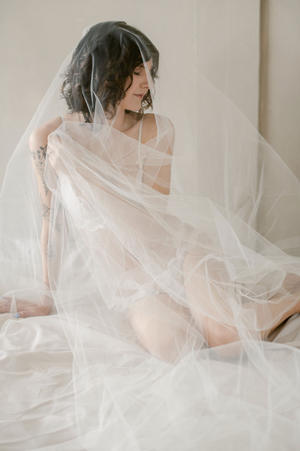 Artistic bridal boudoir photo with flowing white tulle veil creating ethereal romantic mood.