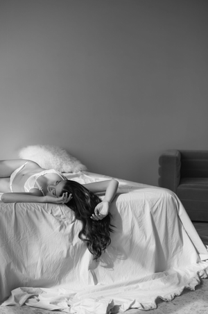 Black and white artistic photograph showing a person lying on white bedding in dramatic lighting.