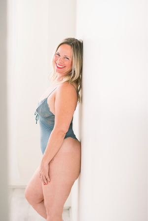 Person wearing a blue bodysuit poses against a white wall in a bright studio setting.