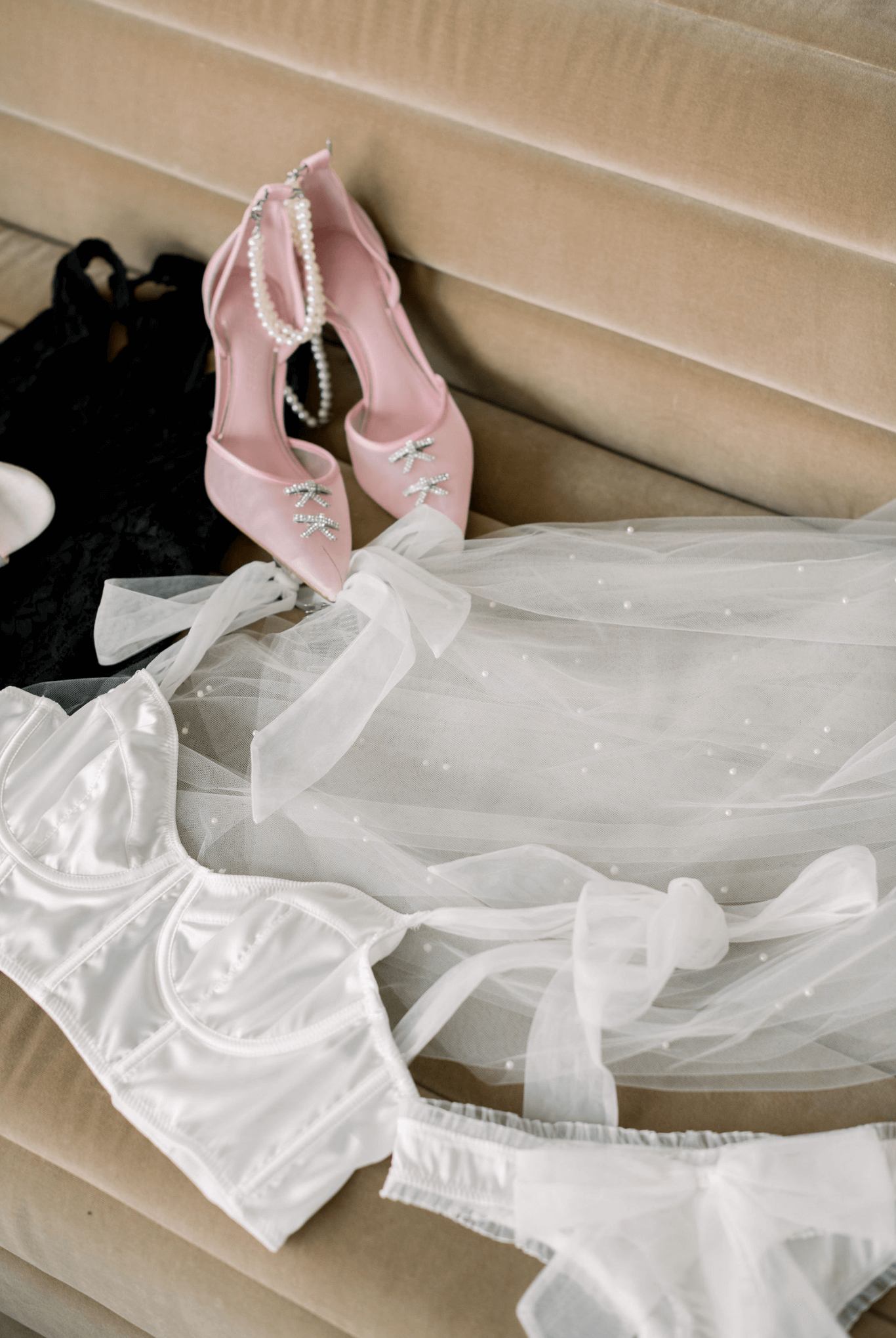 Bridal accessories including pink ballet flats, white corset and tulle fabric laid on beige couch.