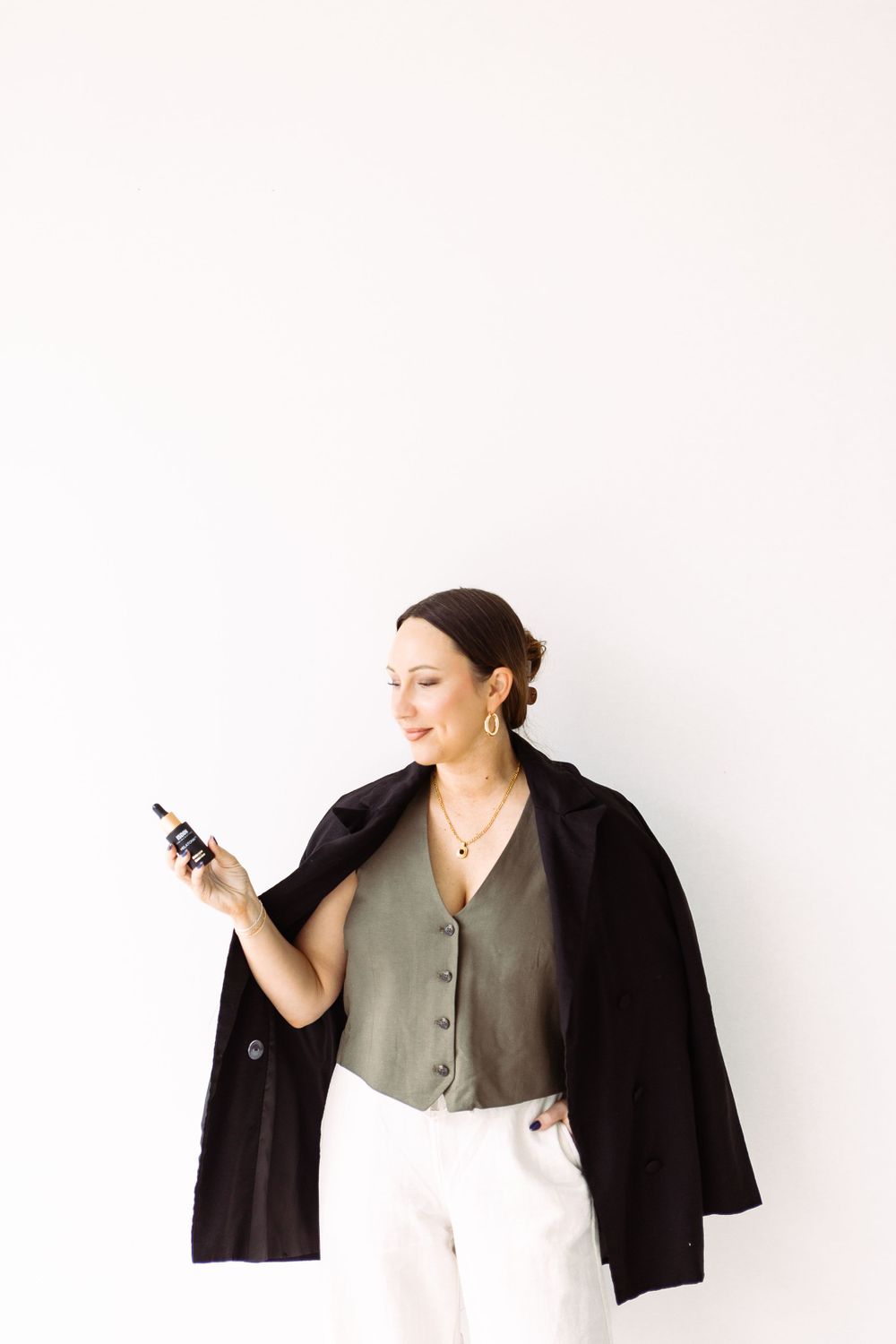 Person in black jacket and olive top posing against white background in minimalist style.