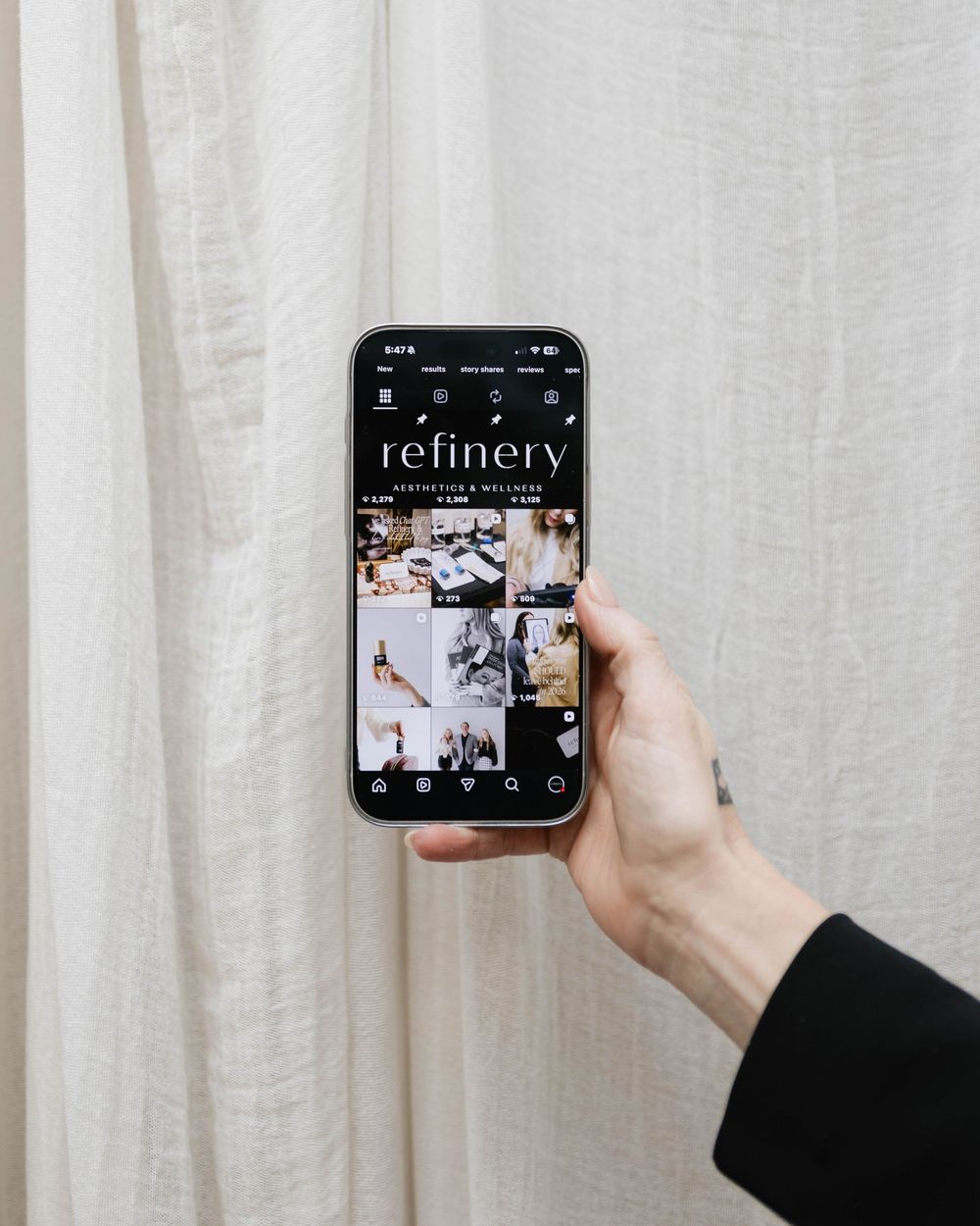 Hand holding phone displaying social media grid against white curtain background.