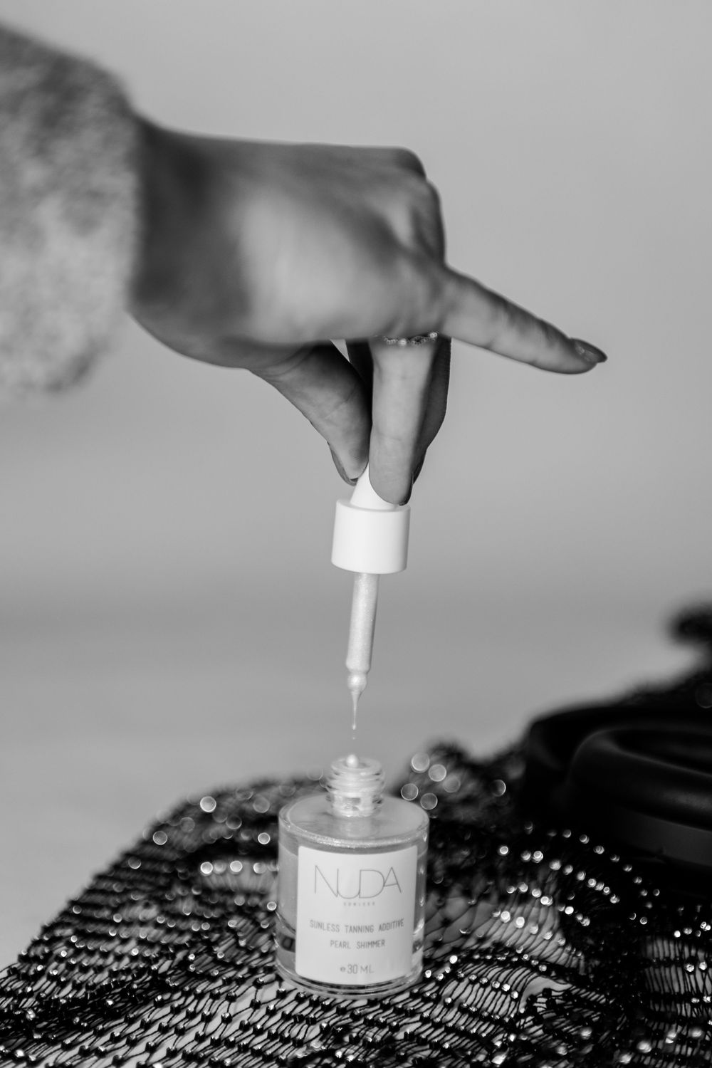 Close-up of a hand applying nail polish or beauty product in black and white.
