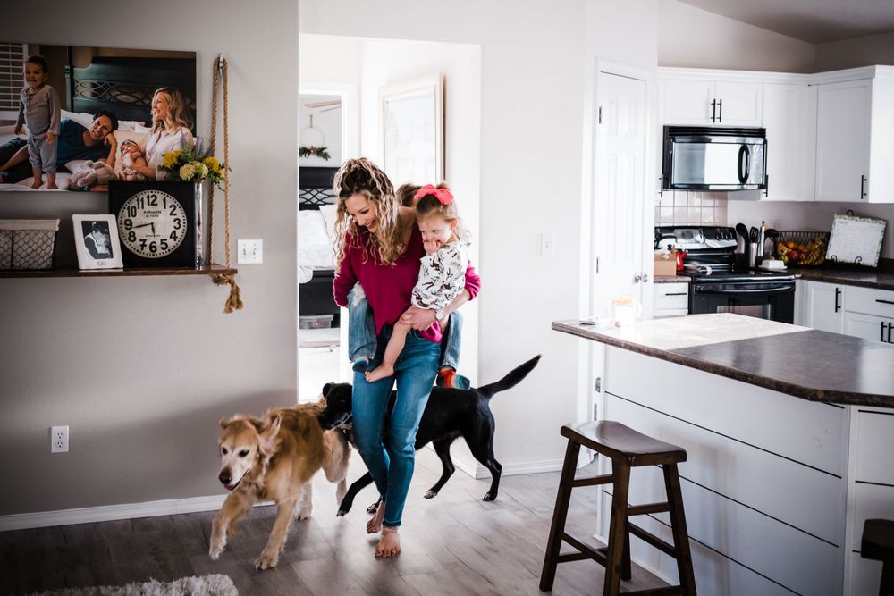 A woman walks through a modern kitchen with two playful dogs while holding a young child.