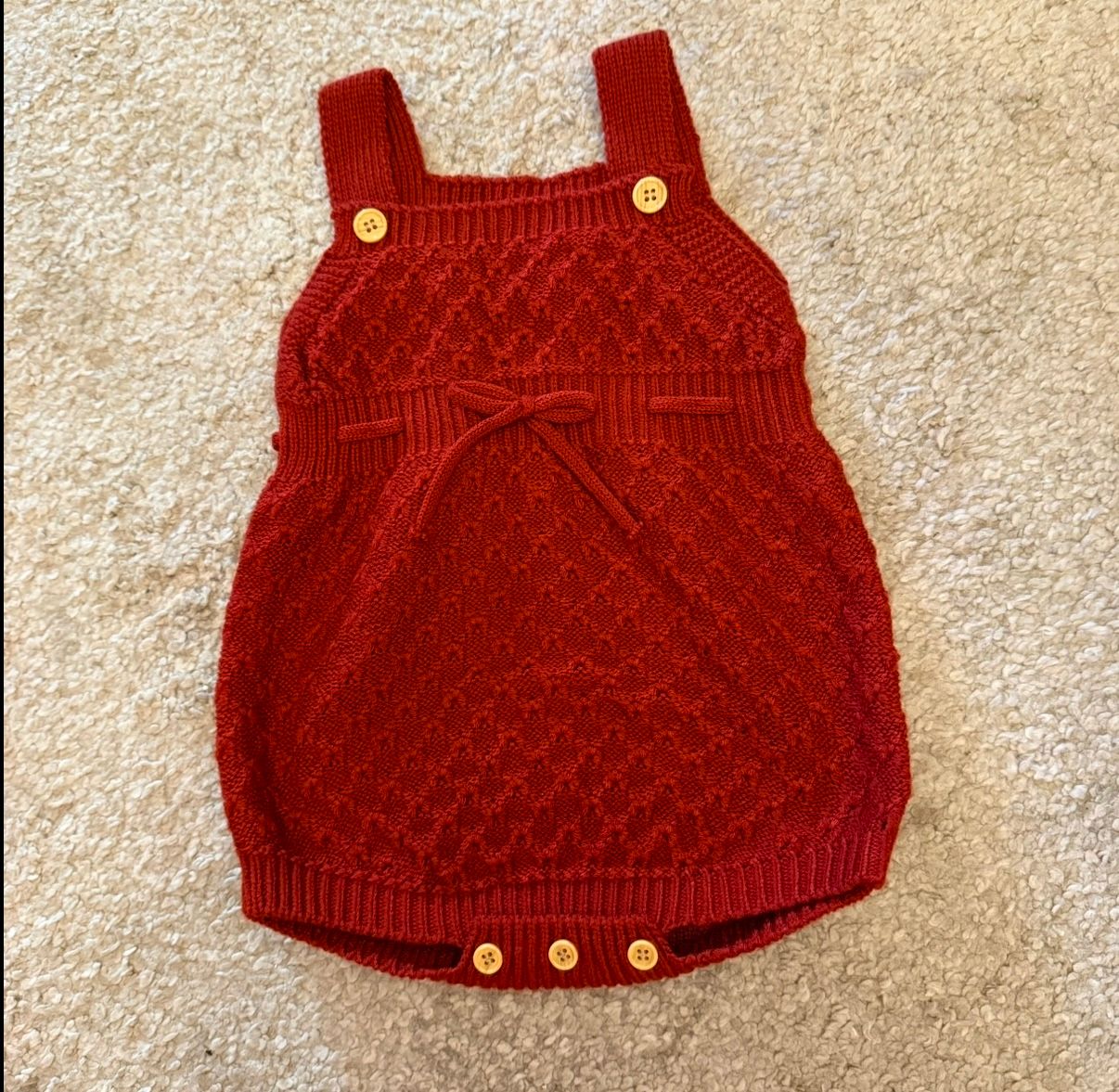 Deep red knitted baby romper with decorative pattern.