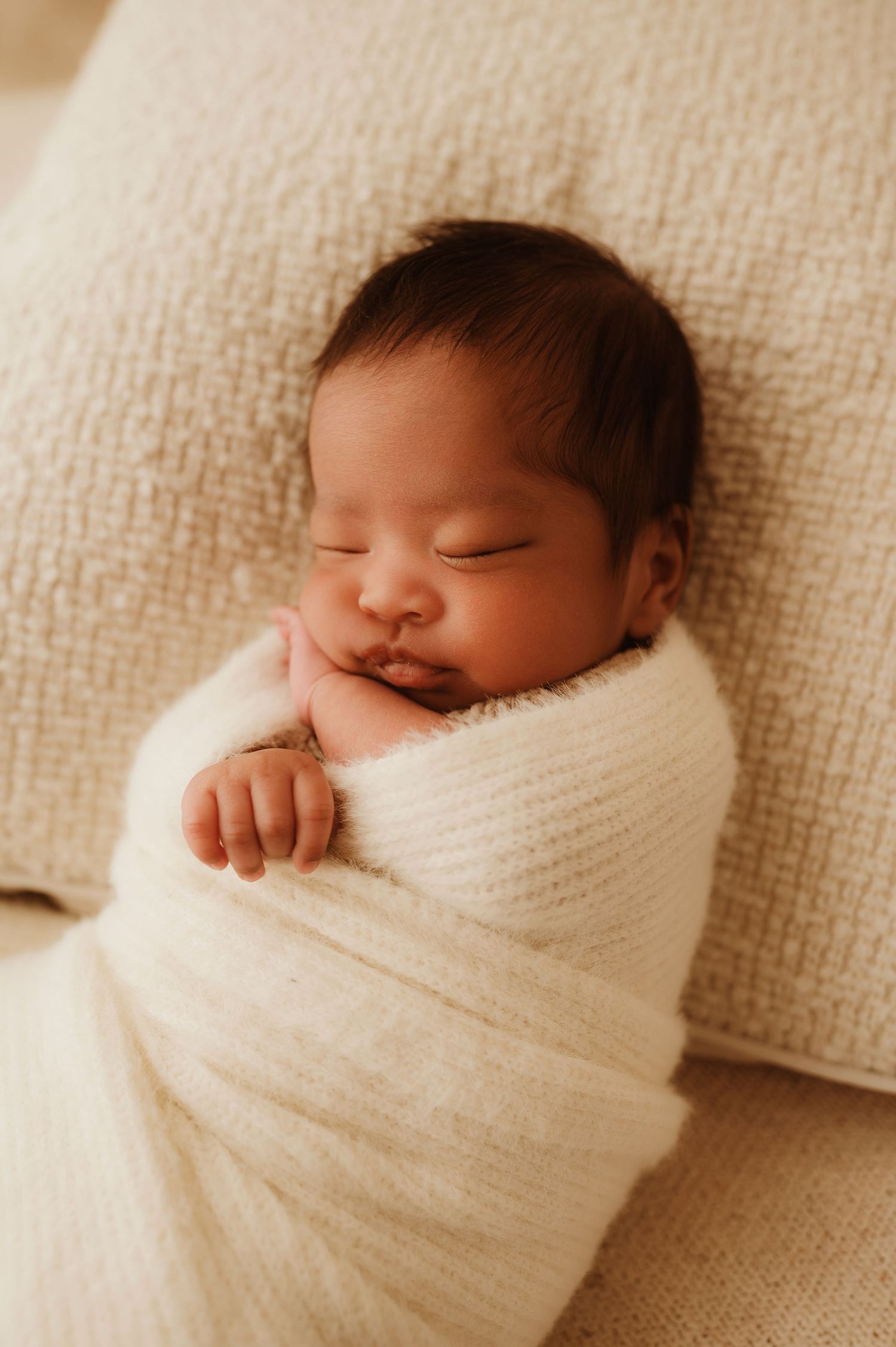 Infant wearing a cozy cream-colored ribbed sweater onesie with wooden buttons while resting on beige textiles.