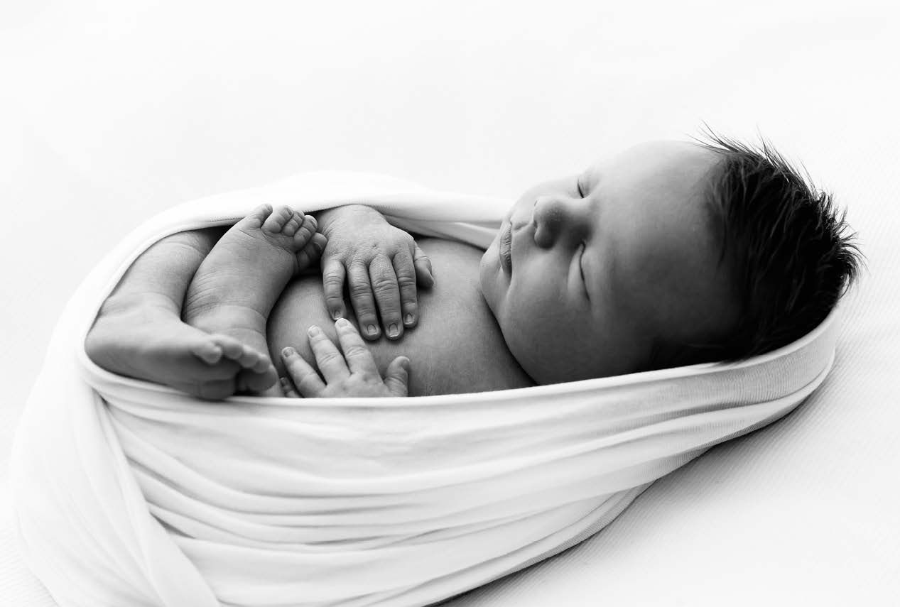 A sleeping newborn baby wrapped in soft white fabric lies peacefully in black and white photography.