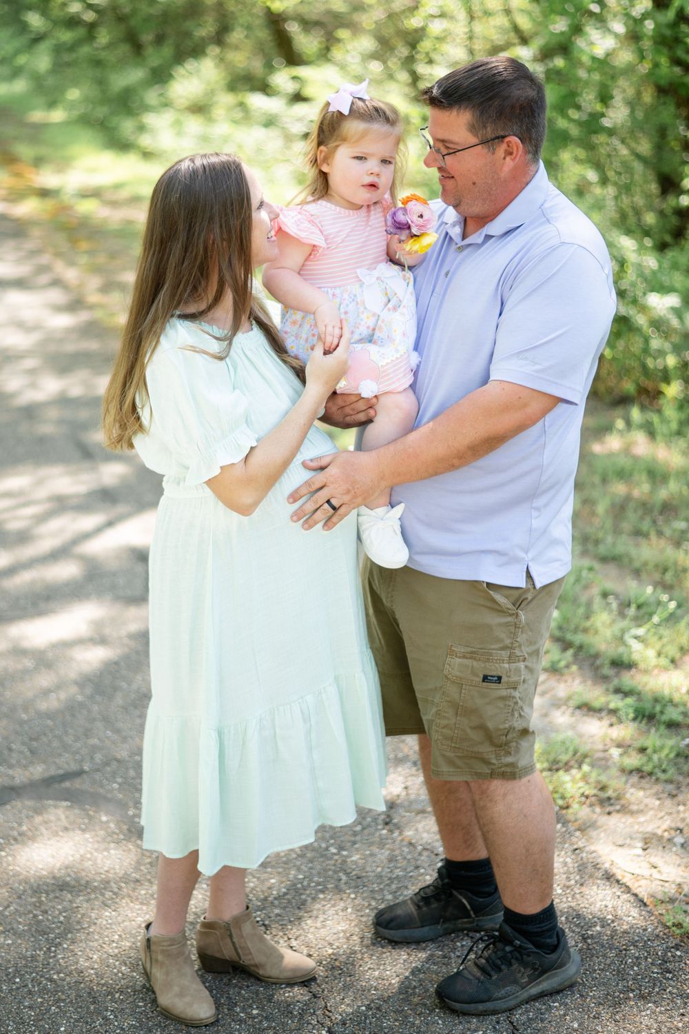 A family shares a tender outdoor moment together on a sunlit path through greenery.
