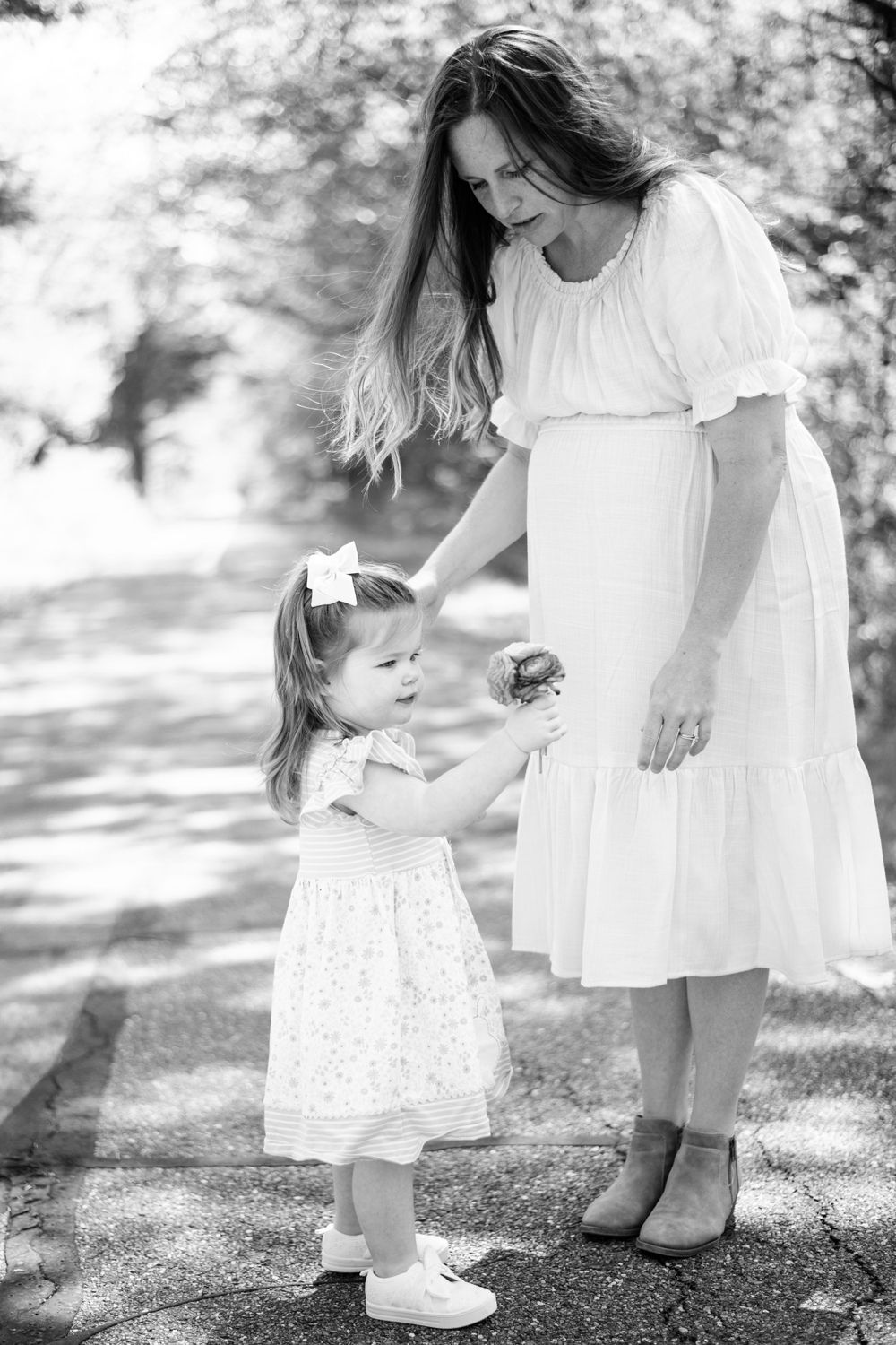 Black and white photo of a parent and small child in white dresses holding hands outdoors on a sunny day.