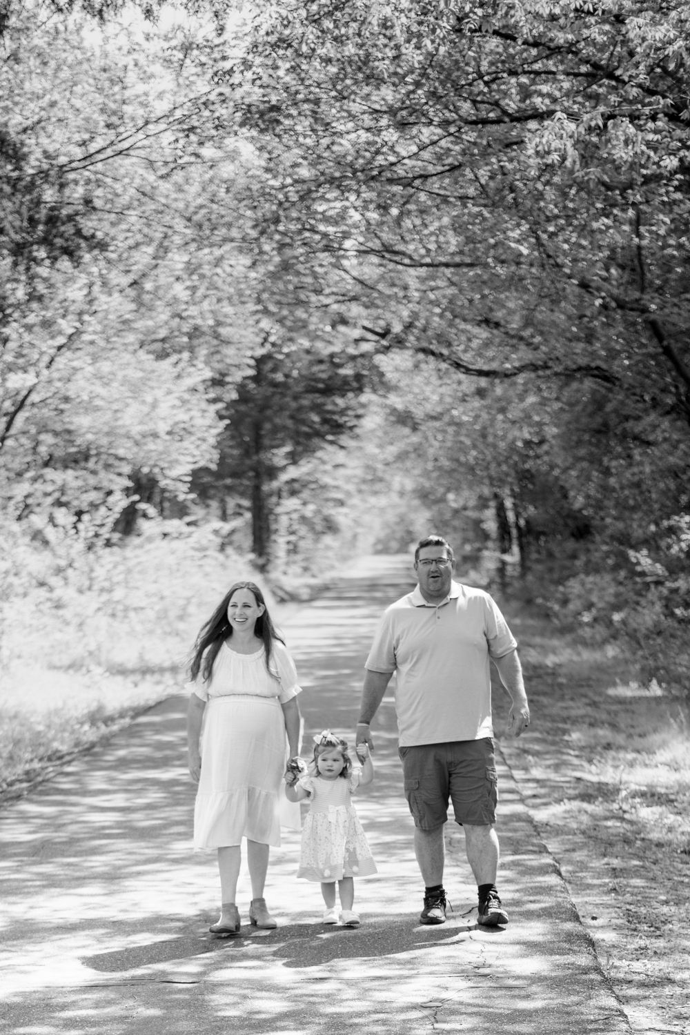 A family takes a peaceful stroll together down a sunlit tree-lined path on a summer day.
