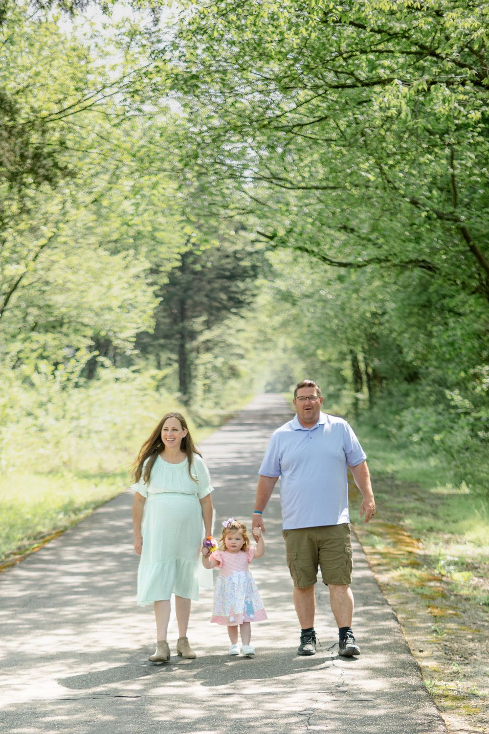A family walks together holding hands on a tree-lined path on a sunny summer day in nature.