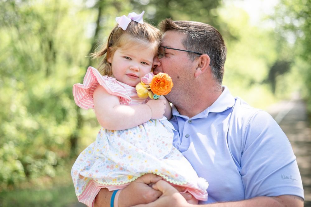 A tender moment shared between parent and child outdoors holding a bright orange flower on a sunny spring day.