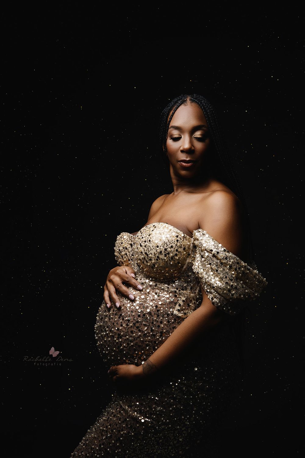 A person in a glamorous sequined gown poses against a dark background in an elegant maternity portrait.
