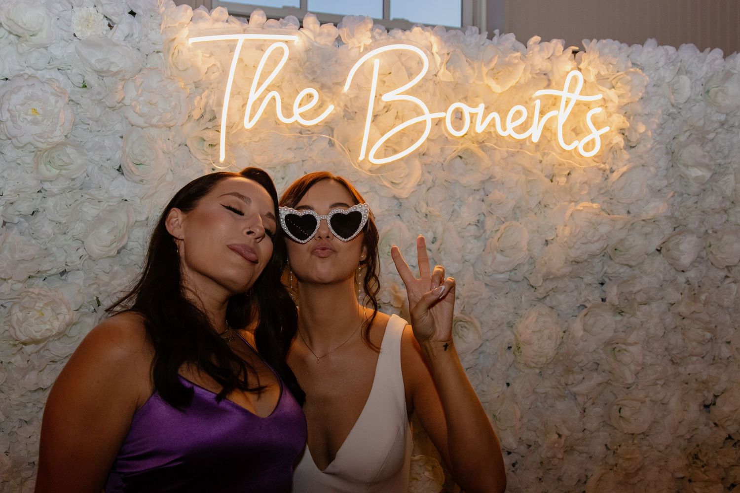 Party guests pose against illuminated neon signage at wedding reception.