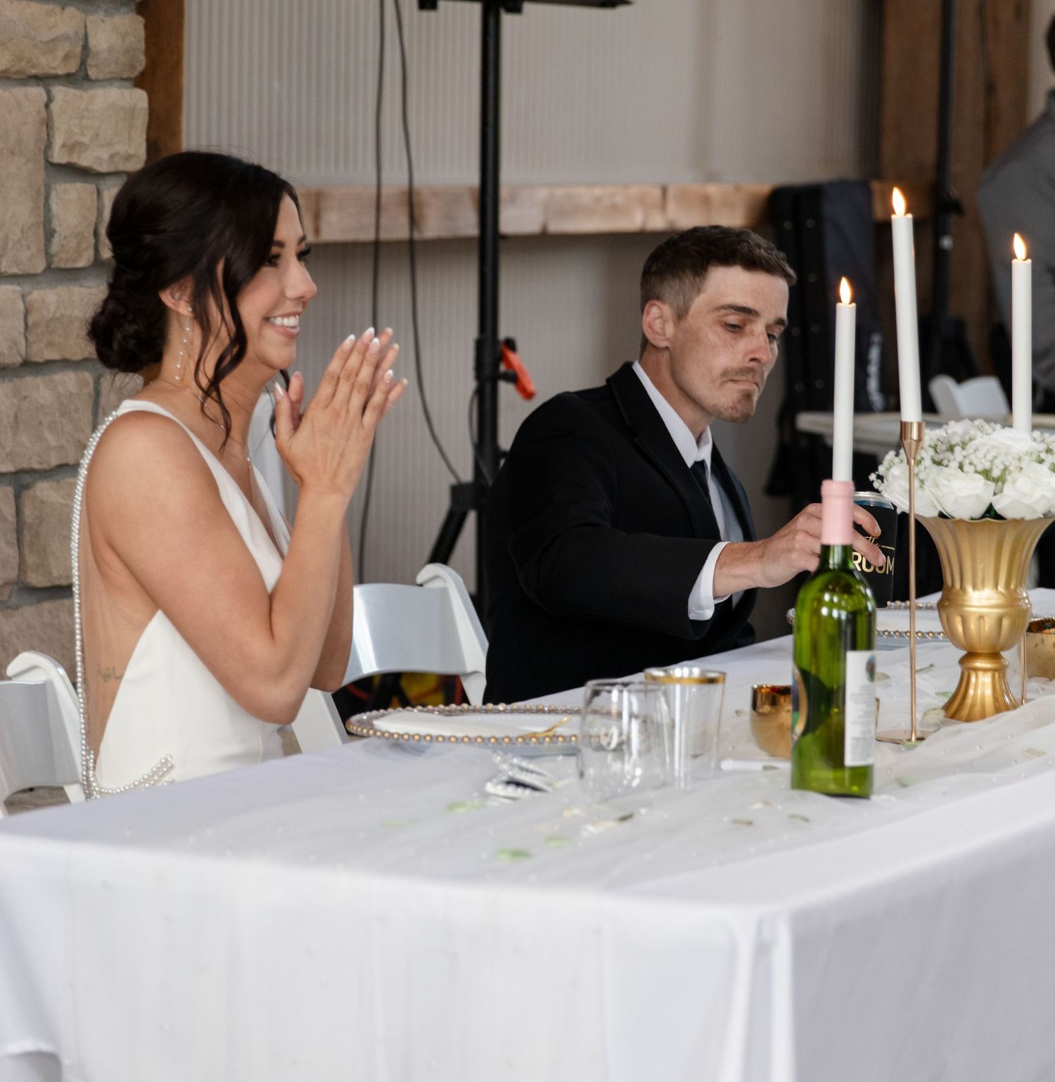 Wedding party sits at an elegant head table decorated with white linens and candlesticks.