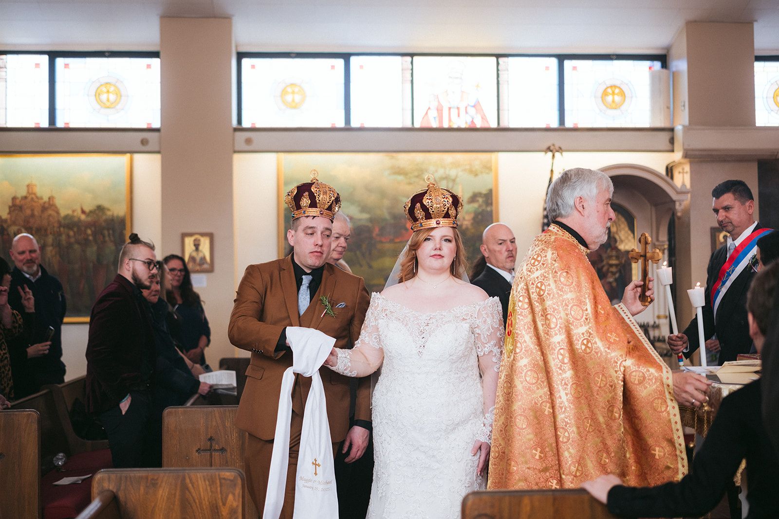 A traditional religious ceremony takes place in a church with gold-robed clergy and wedding attendees standing in the pews.