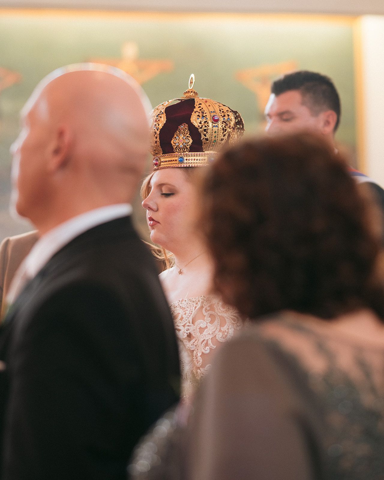A bride wearing an ornate gold crown and lace dress stands among guests during a wedding ceremony celebration.
