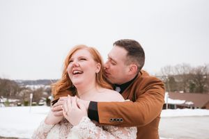 A couple shares a joyful embrace while laughing together in a snowy winter landscape.