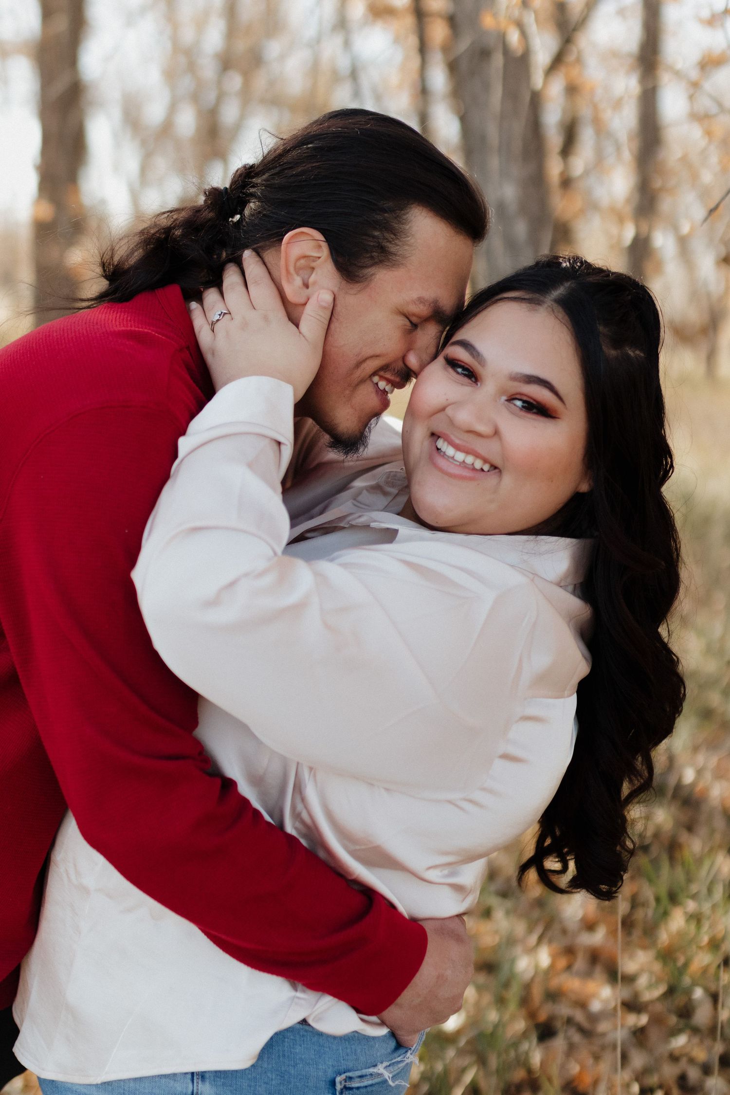 A couple embraces intimately in an autumn forest setting wearing red and white sweaters.
