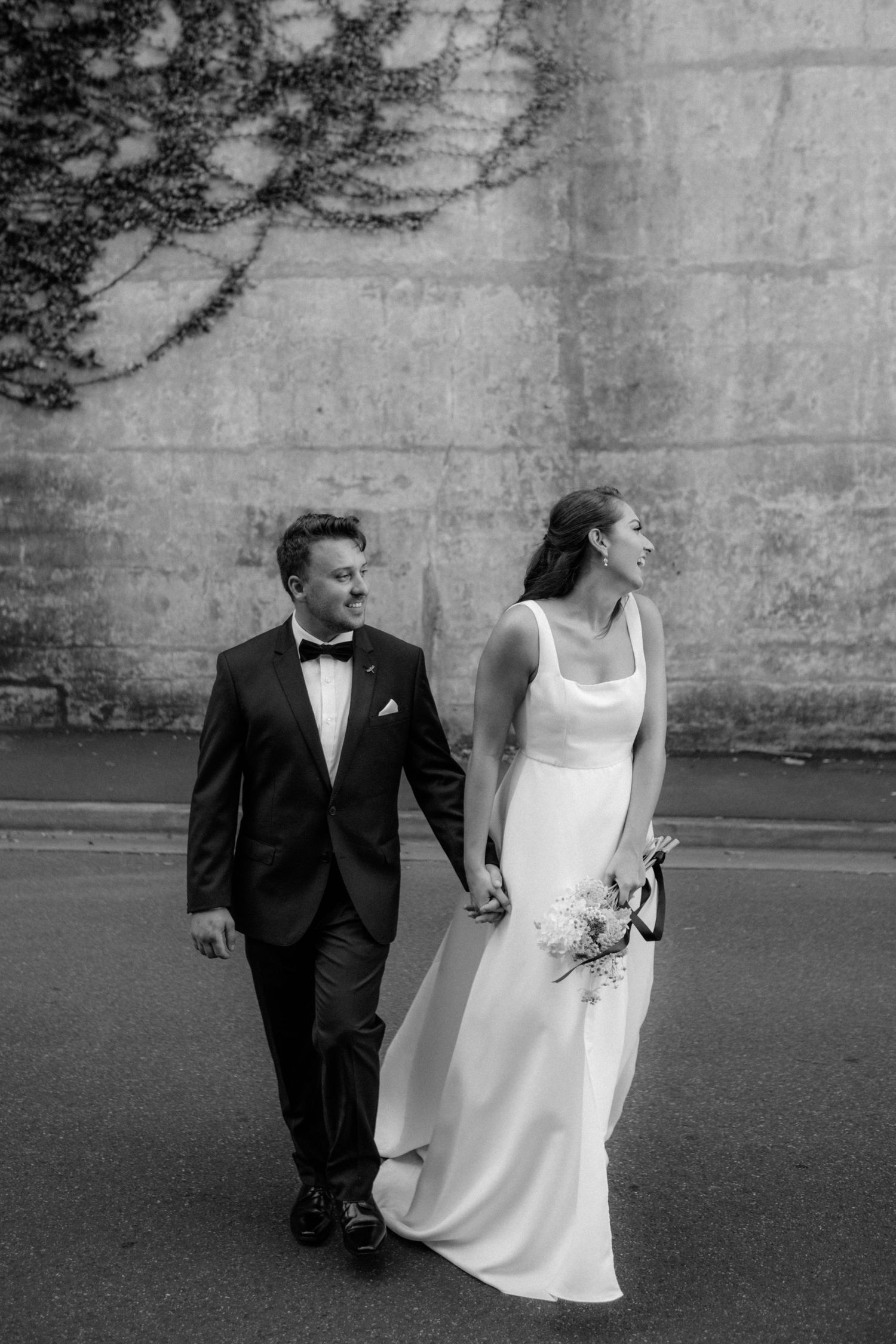 Black and white wedding photo showing couple walking together, bride in elegant white dress with bouquet and groom in tuxedo.