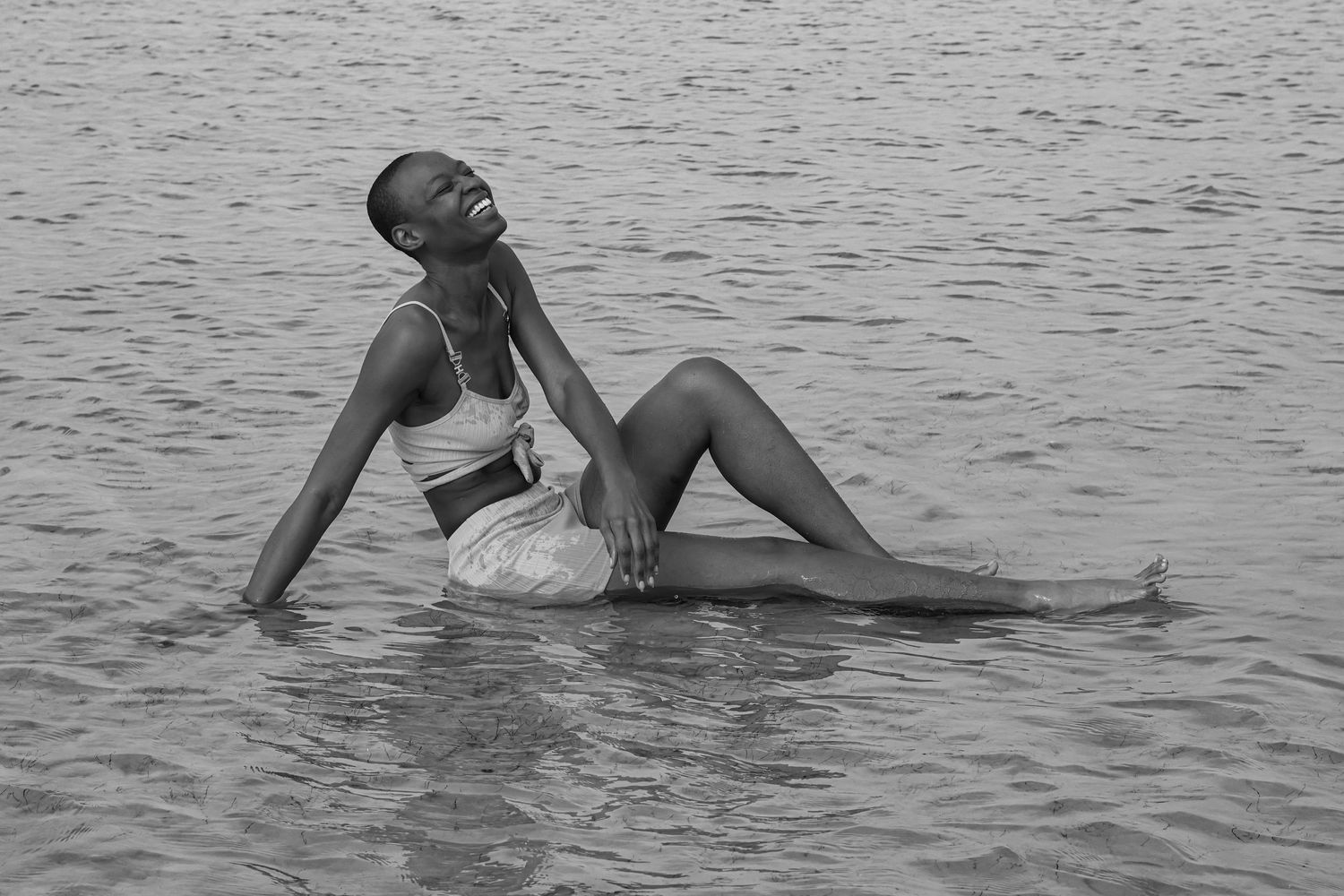 A figure lounges gracefully in shallow water outside Tampa, Florida; wearing a bright bikini in this artistic black and white photograph.