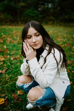 Autumn portrait session showing someone in white jacket and jeans sitting among fallen leaves.