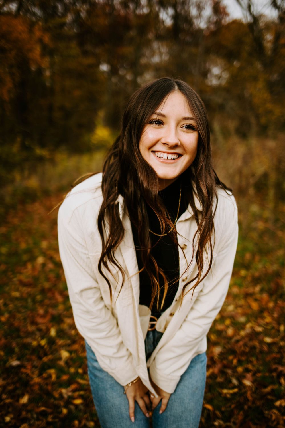 A casual outdoor portrait session featuring someone in a white jacket and jeans amid fall foliage.