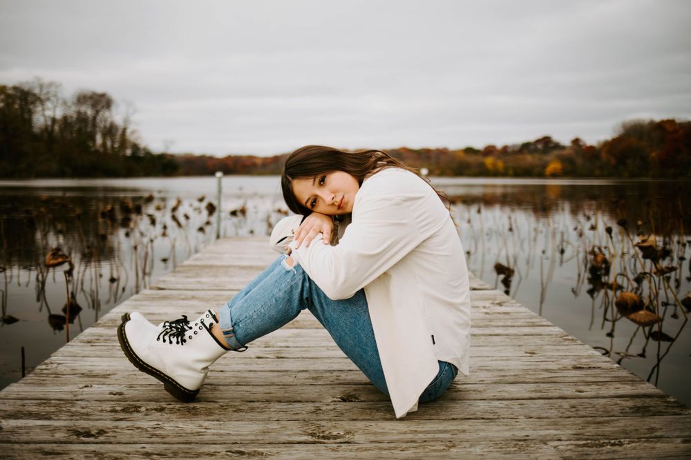 Someone lies on a wooden dock overlooking a serene lake during an overcast day.