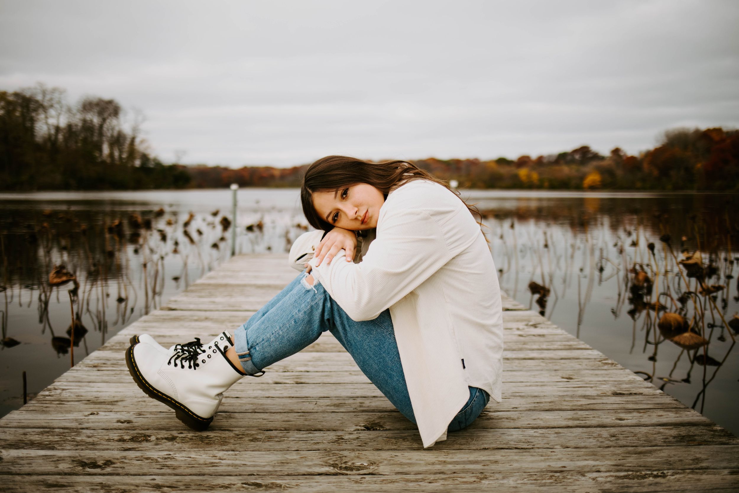 Someone lies on a wooden dock overlooking a serene lake during an overcast day.