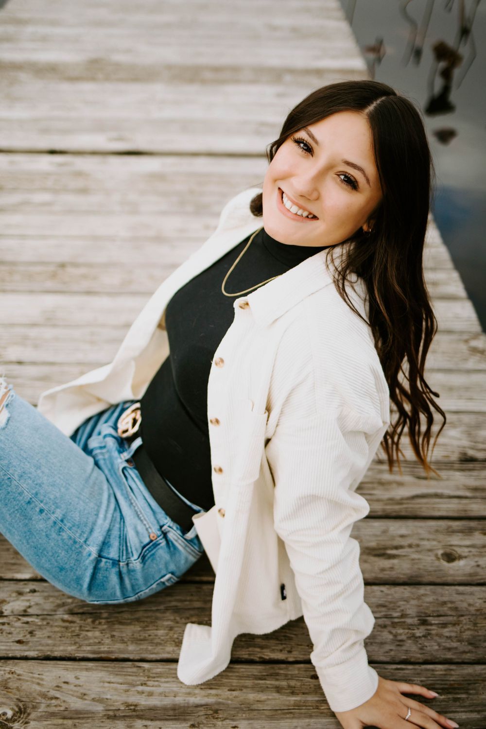 A playful pose on a wooden dock wearing a white jacket and blue jeans.