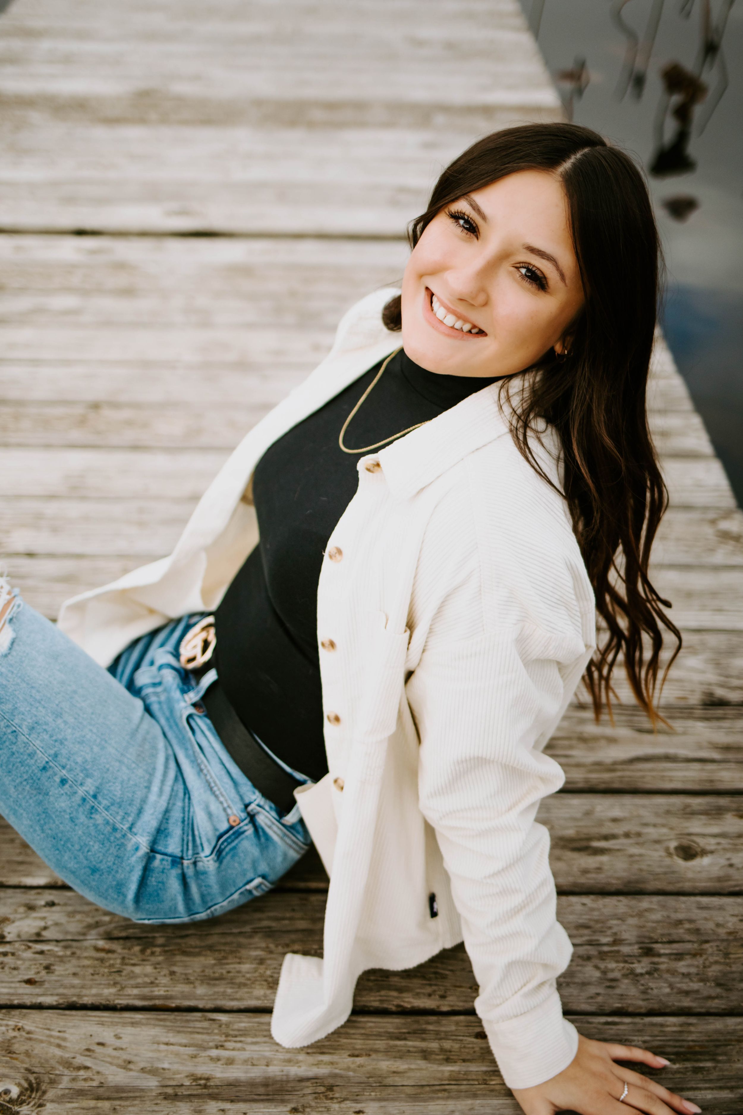 A playful pose on a wooden dock wearing a white jacket and blue jeans.