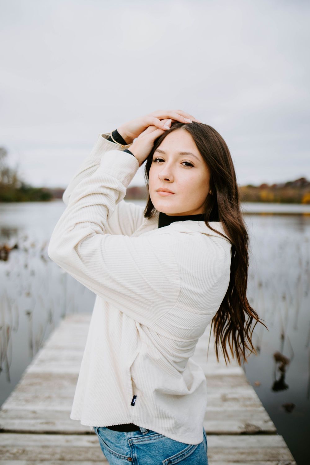 Portrait session by the water featuring casual poses in a white jacket and jeans.