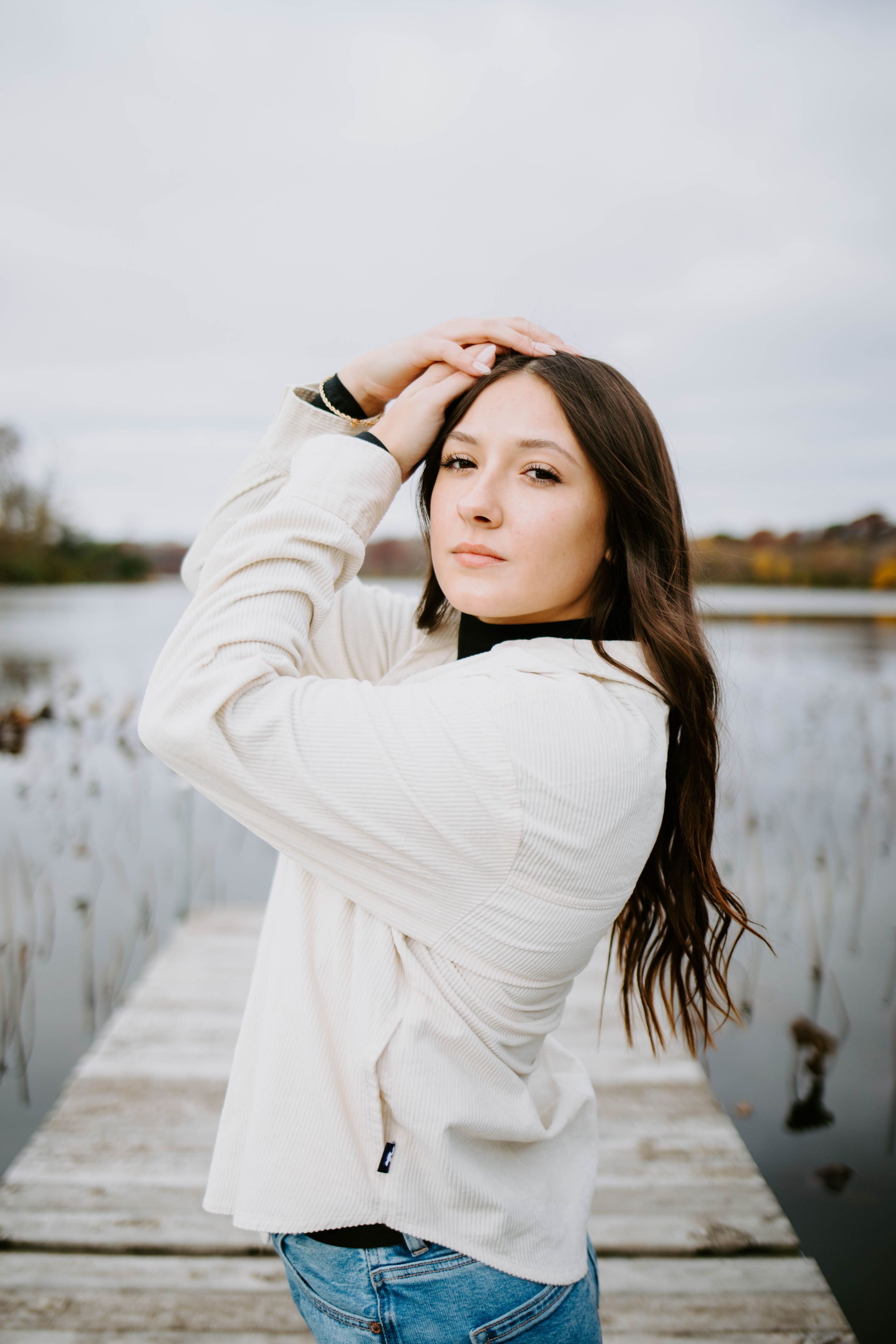 Portrait session by the water featuring casual poses in a white jacket and jeans.
