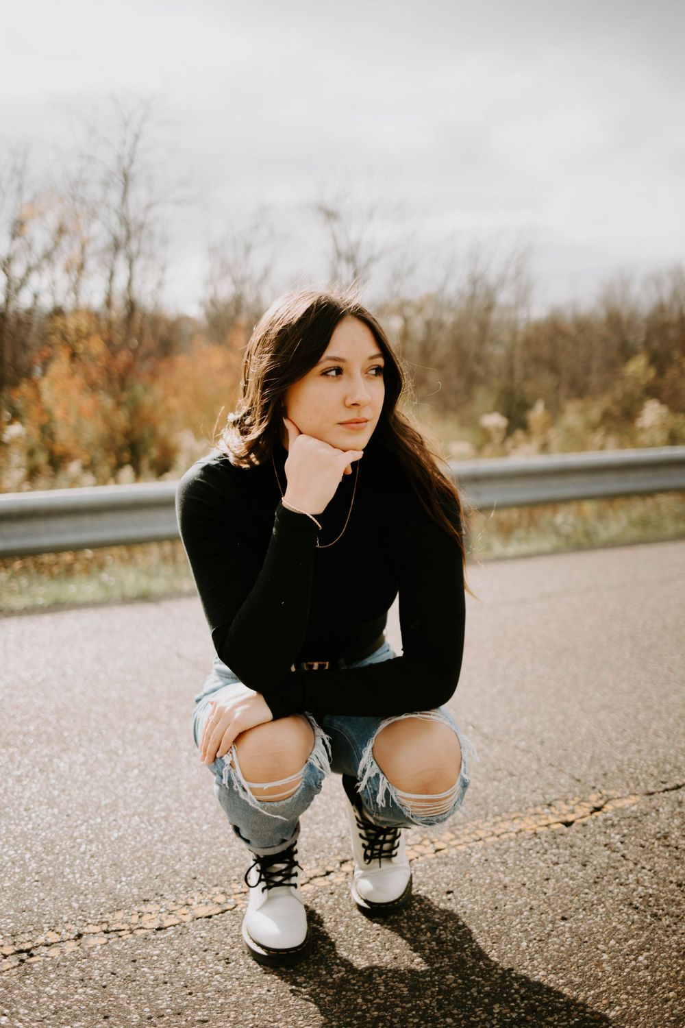 Someone crouches on asphalt wearing ripped jeans and sneakers during an outdoor photo session.