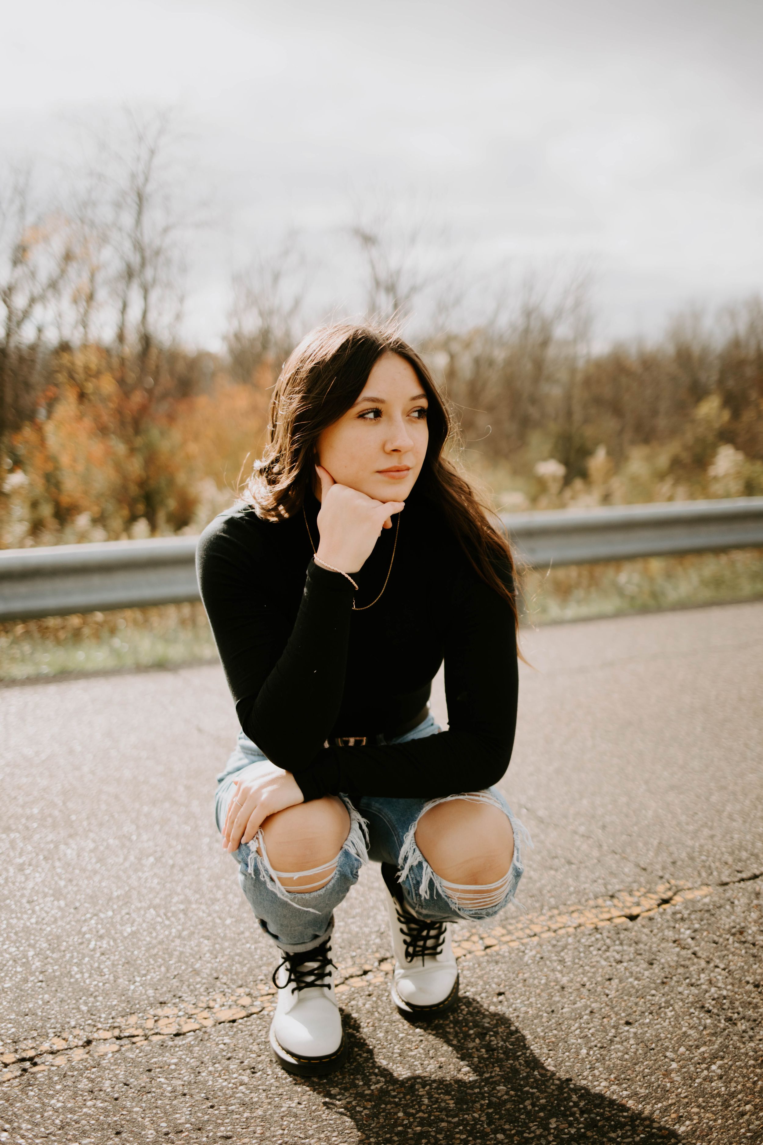 Someone crouches on asphalt wearing ripped jeans and sneakers during an outdoor photo session.