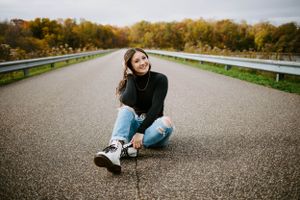 Person in casual wear sitting on a paved road during autumn.