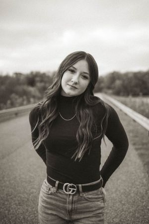 Portrait series on a paved road wearing black turtleneck and designer belt.