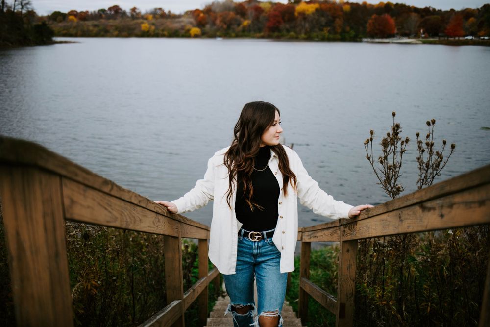 Someone stands on a wooden boardwalk overlooking an autumn lake landscape.