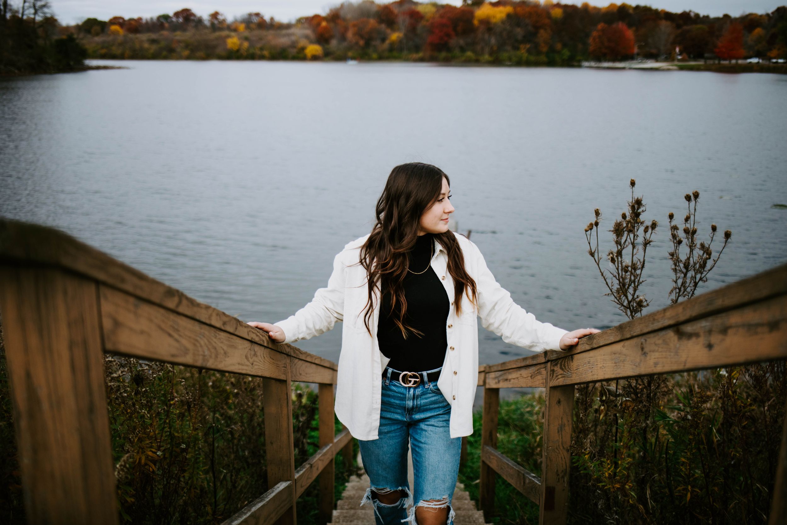 Someone stands on a wooden boardwalk overlooking an autumn lake landscape.