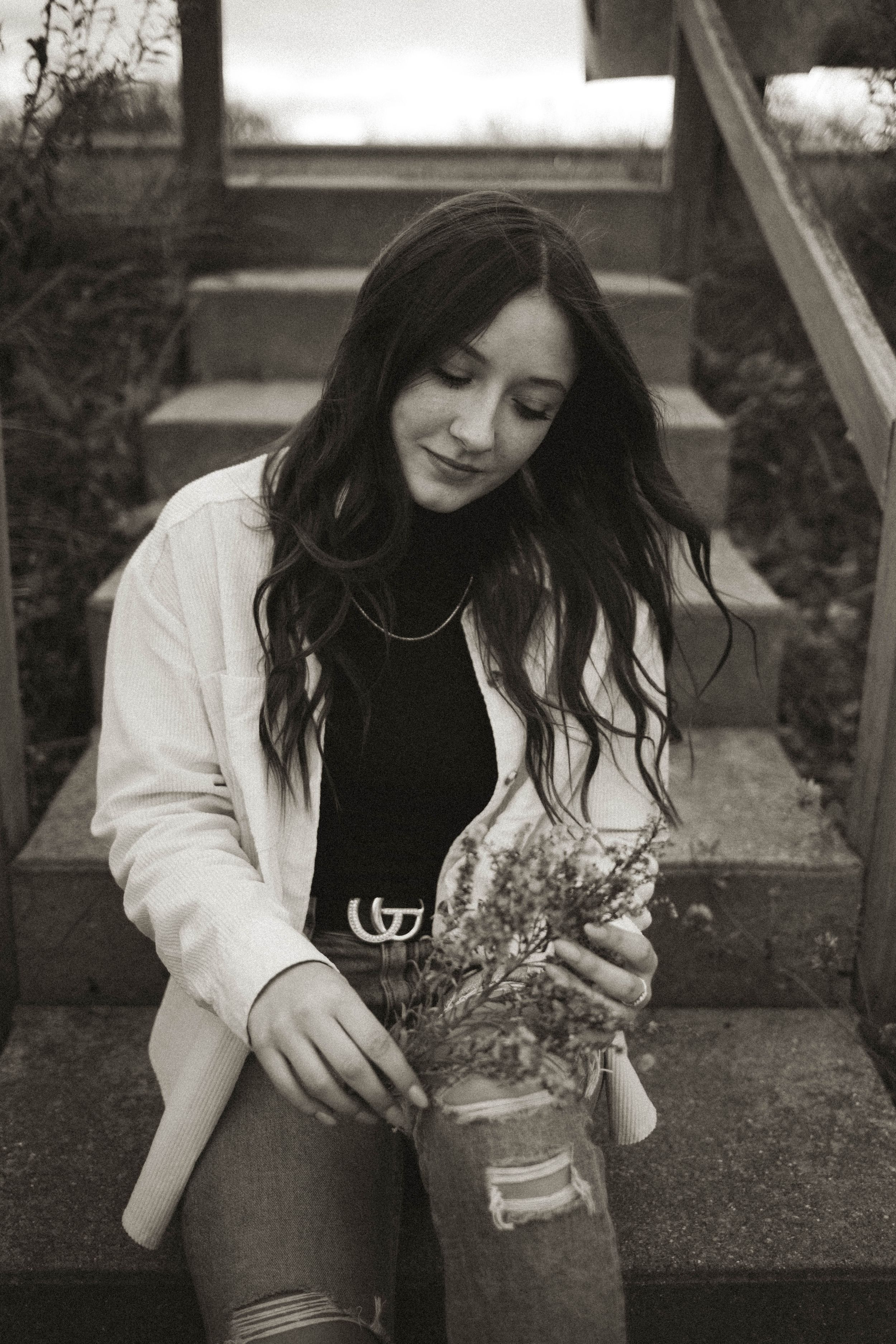 A black and white portrait with someone holding dried flowers on outdoor steps.