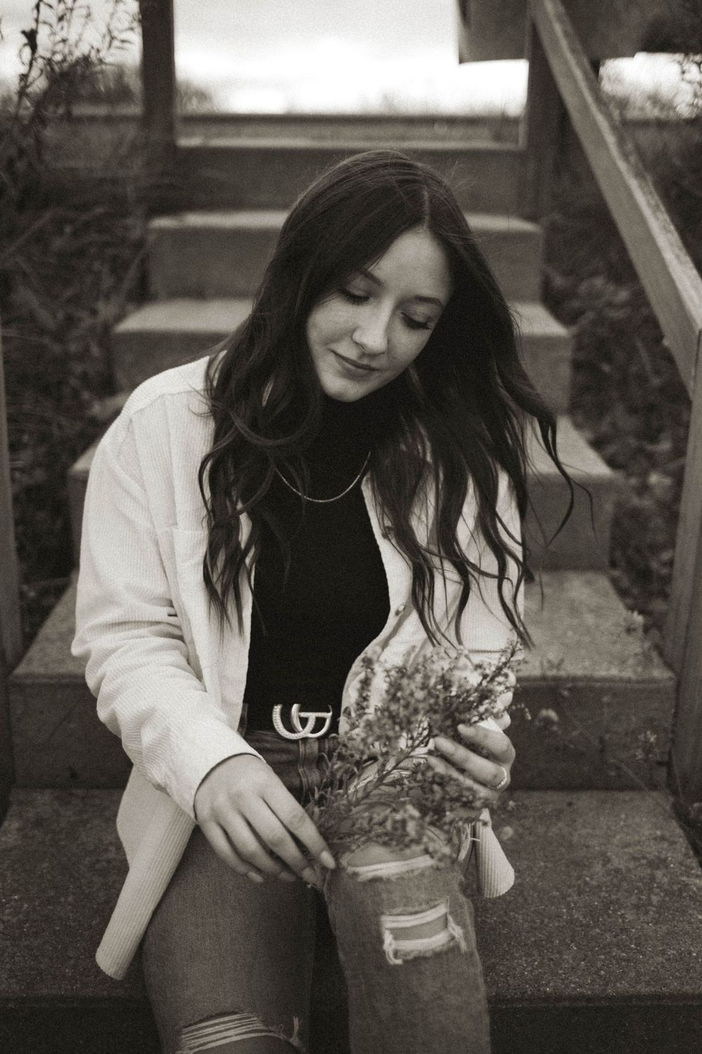 A black and white portrait with someone holding dried flowers on outdoor steps.