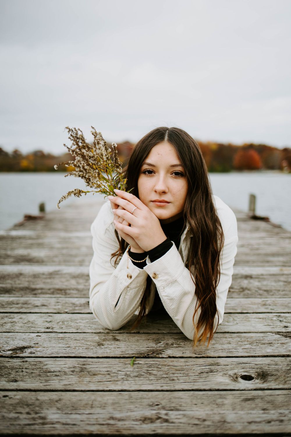 Artistic portrait series of someone lying on a wooden dock with dried flowers during autumn.