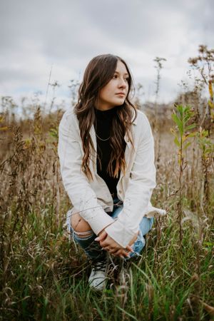 Person in white jacket sitting among tall wildflowers in a natural outdoor setting.