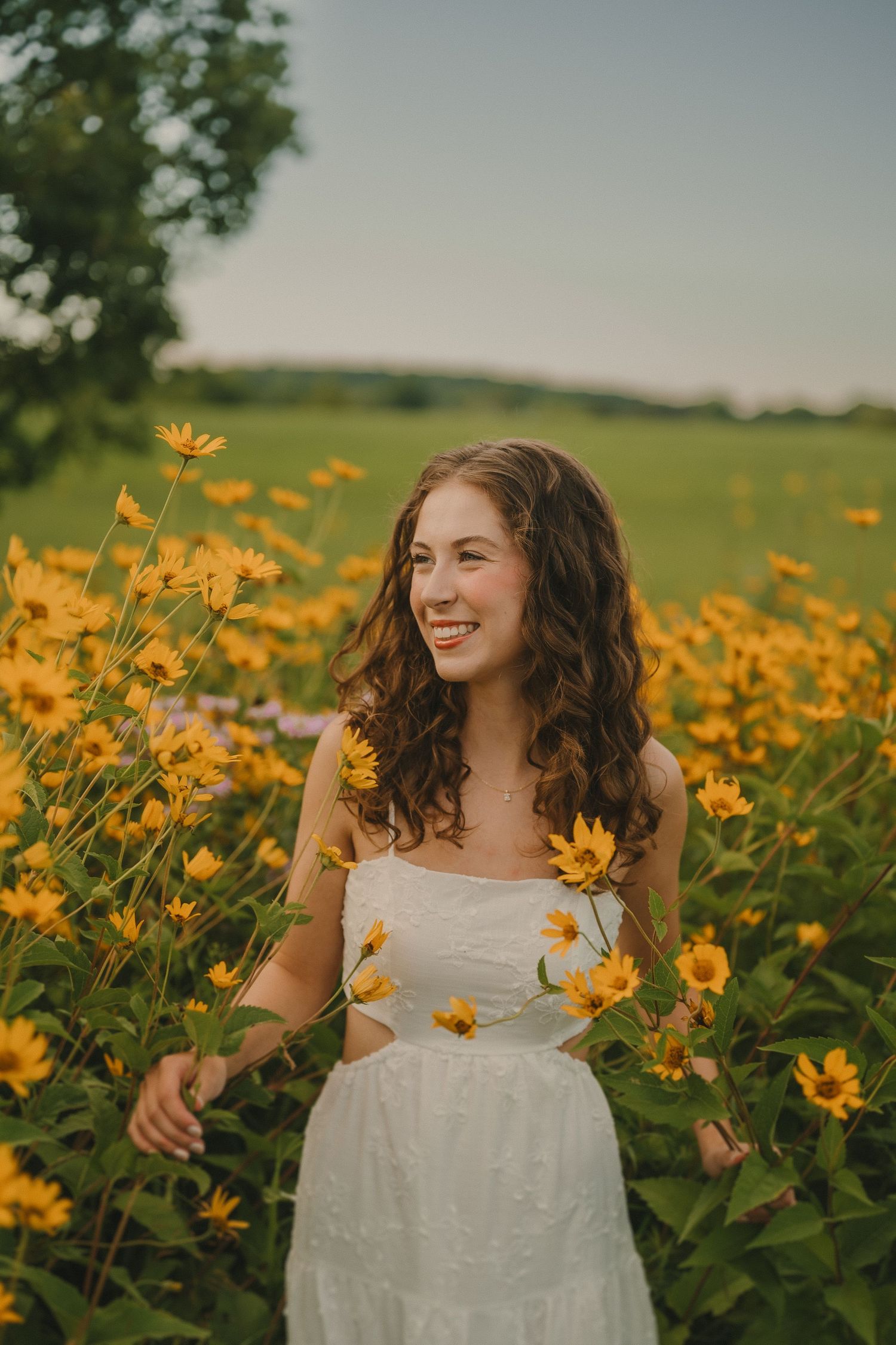 A white dress-clad person stands among vibrant yellow wildflowers in a sunny meadow at golden hour.