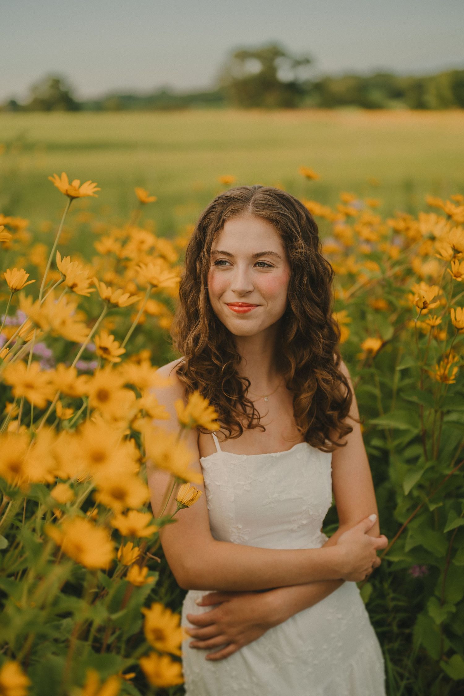 A portrait of someone in a white dress standing among vibrant yellow wildflowers in a sunny meadow.
